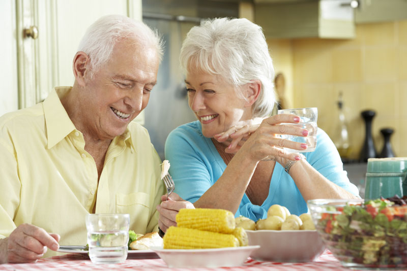 an older couple smiling at one another over the dinner table because they are happy they considered getting implant supported dentures to improve their smile.