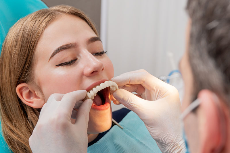 a dental patient in a procedure chair as her oral surgeon improves her smile by placing her temporary prosthesis during her full mouth dental implant procedure.
