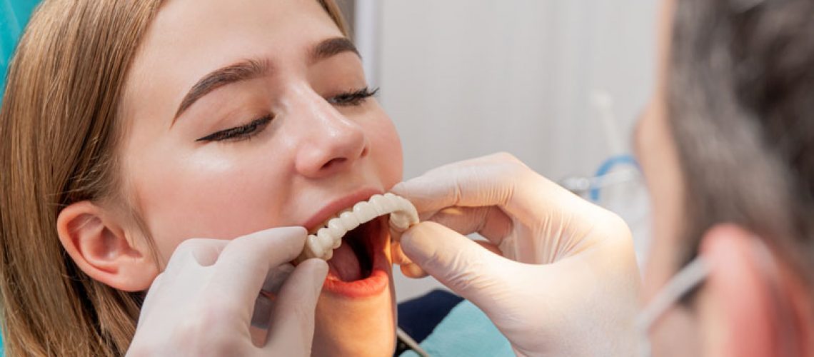 a dental patient in a procedure chair as her oral surgeon improves her smile by placing her temporary prosthesis during her full mouth dental implant procedure.