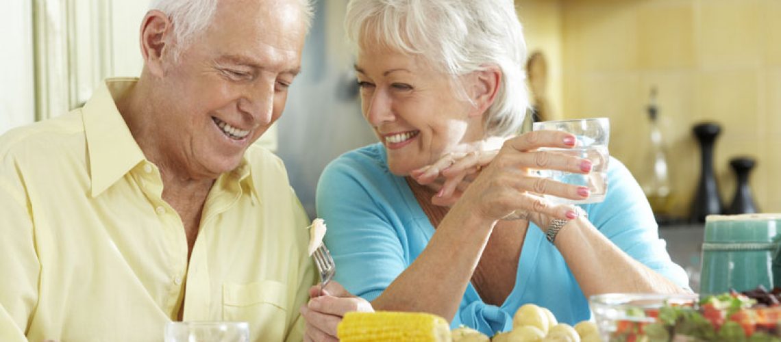an older couple smiling at one another over the dinner table because they are happy they considered getting implant supported dentures to improve their smile.